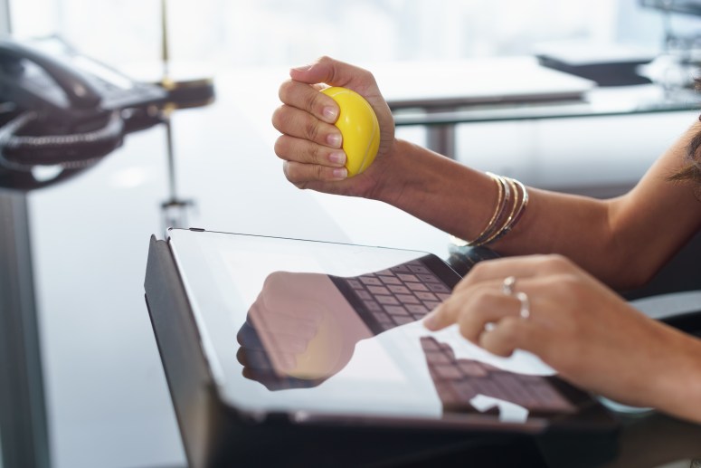 Stressed office worker with anti stress ball types email